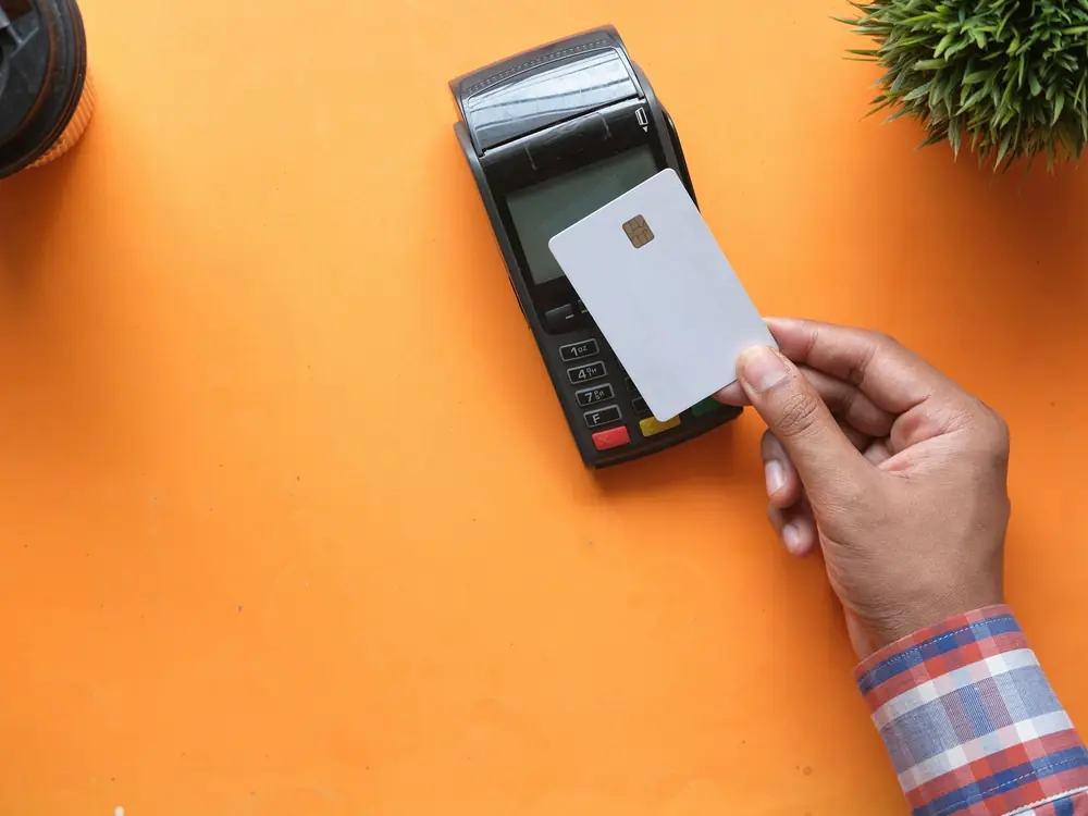 Bankkarte wird an ein Kartenterminal auf orangefarbenem Grund gehalten